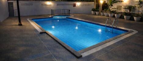 Una piscina rettangolare con bordo piastrellato, circondata da un muretto basso con piante in vaso e luci a parete.