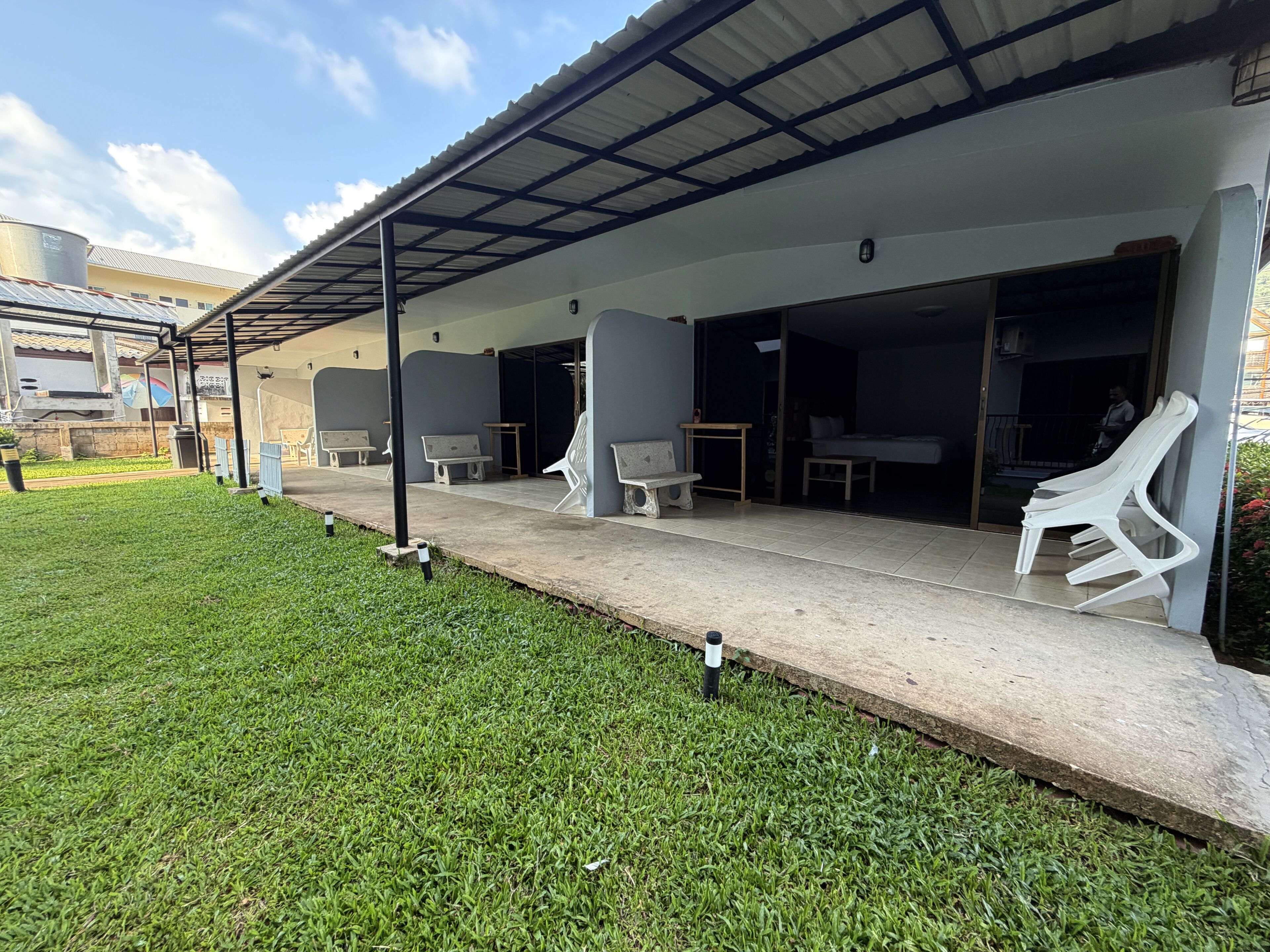 Un espace extérieur aménagé, abrité et doté de chaises et de tables, une pelouse verdoyante et un bâtiment avec un toit en métal.