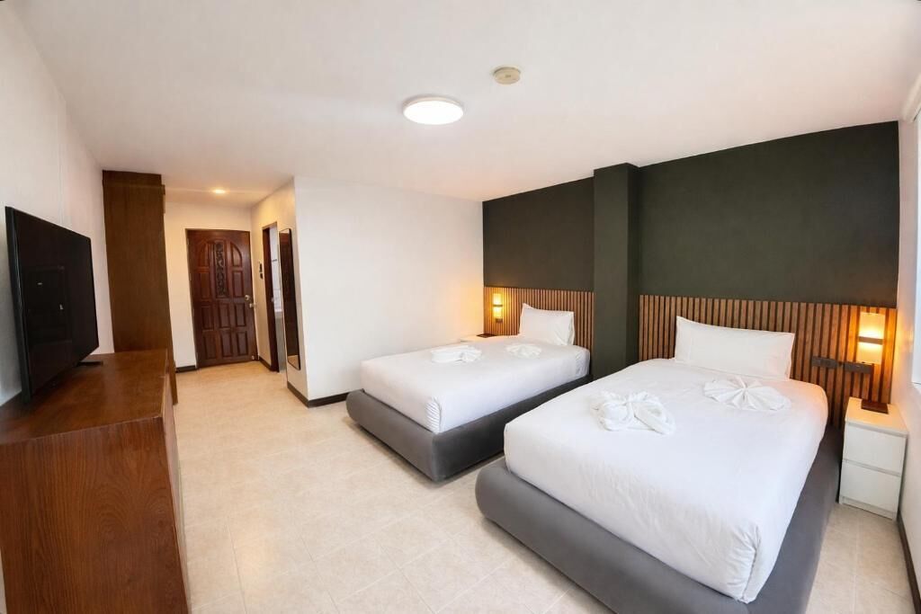 A hotel room with two beds, a TV, a wooden desk, and a hallway leading to another room.