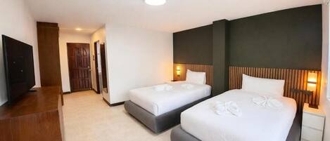 A hotel room with two beds, a TV, a wooden desk, and a hallway leading to another room.