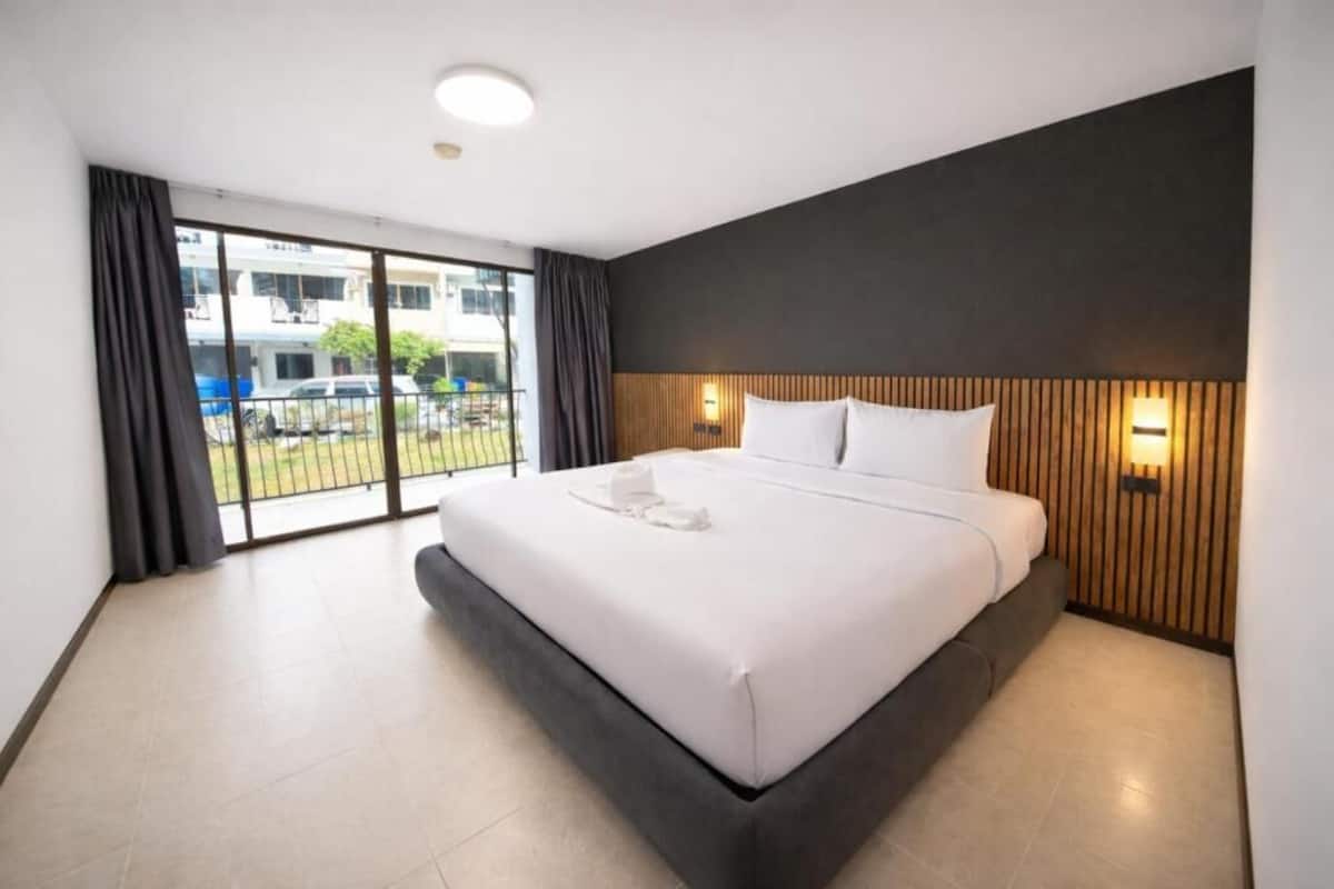 A modern hotel room with a large bed, a balcony with a view, and a wooden headboard.