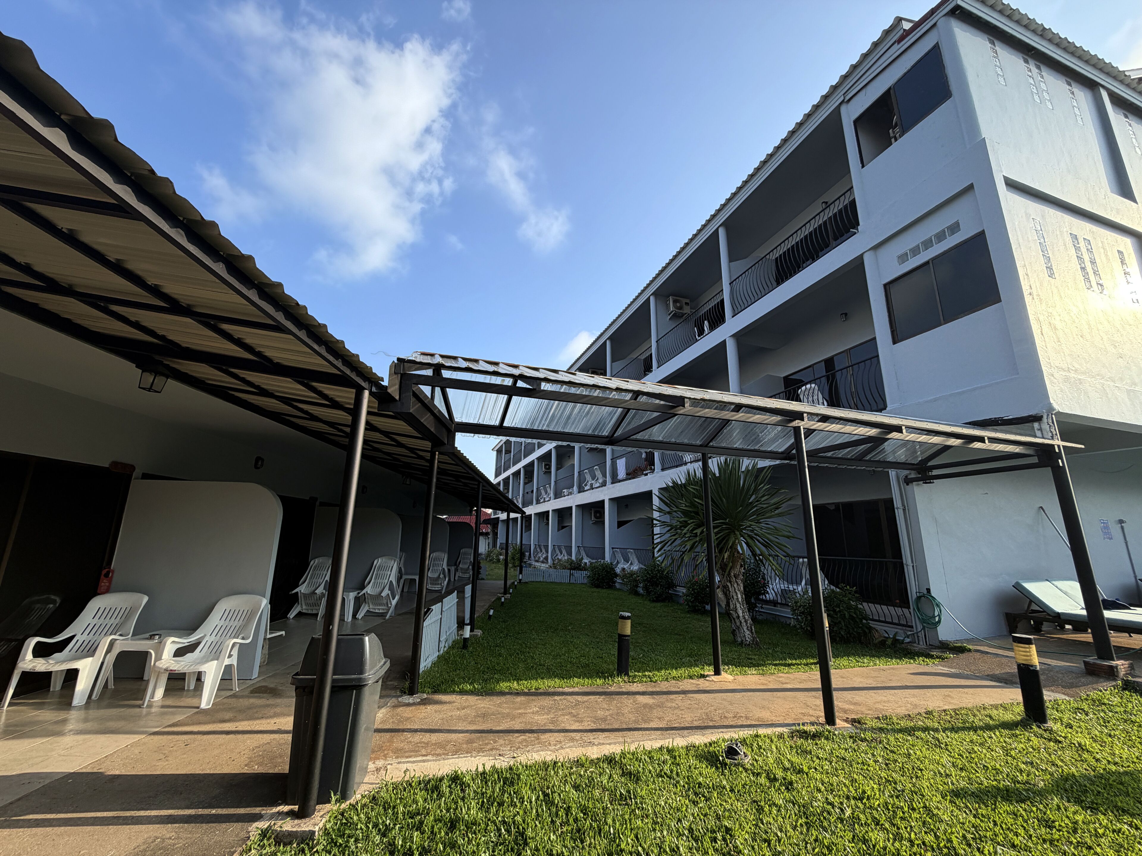 A building with a covered outdoor seating area, a grassy lawn, and a multi-story structure with balconies.