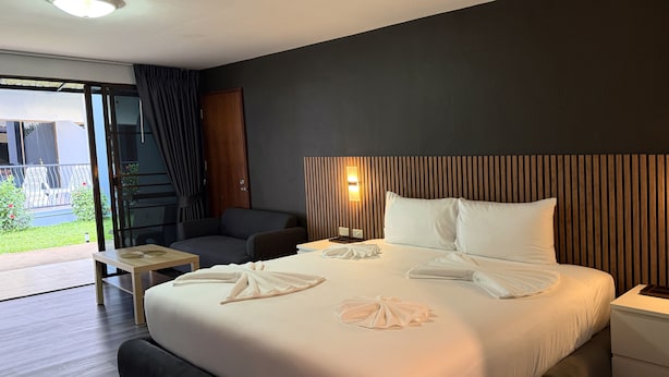 A hotel room with a bed, a bedside table, a chair, a small table, and a view of the outdoors.