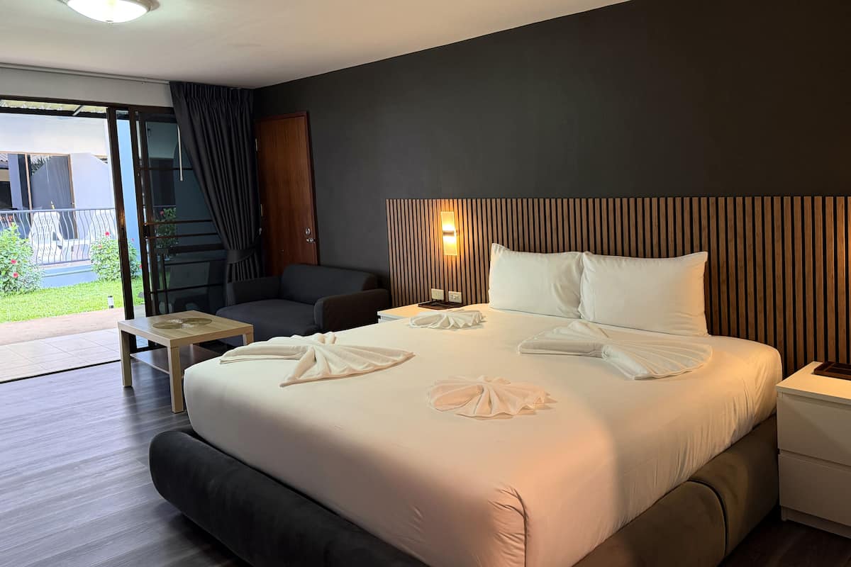 A hotel room with a bed, a bedside table, a chair, a small table, and a view of the outdoors.