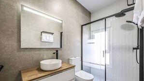 A modern bathroom with a round sink, a mirror, a toilet, and a glass-enclosed shower.