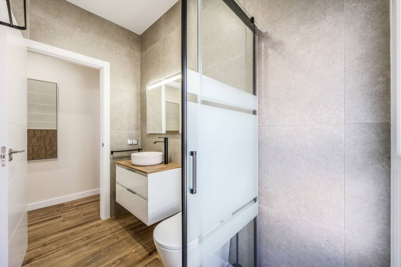 Un baño moderno con cabina de ducha de vidrio, un lavabo blanco y un mueble de tocador de madera.