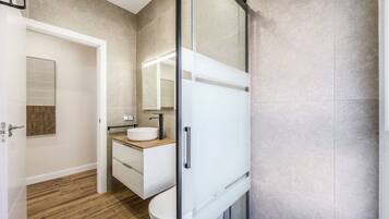 Un baño moderno con cabina de ducha de vidrio, un lavabo blanco y un mueble de tocador de madera.