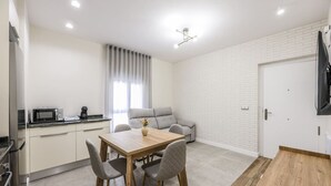 A modern kitchen with a microwave, a dining table with chairs, a sofa, and a TV mounted on the wall.