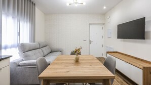 A modern living room with a sofa, a wooden dining table, and a TV mounted on the wall.