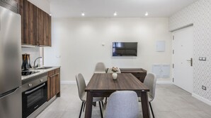 Una cocina moderna con horno integrado, un comedor con mesa y sillas de madera, un televisor de pantalla plana montado en la pared y un papel tapiz estampado.