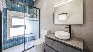 Un baño moderno con cabina de ducha de vidrio, un lavamanos blanco y un espejo grande.