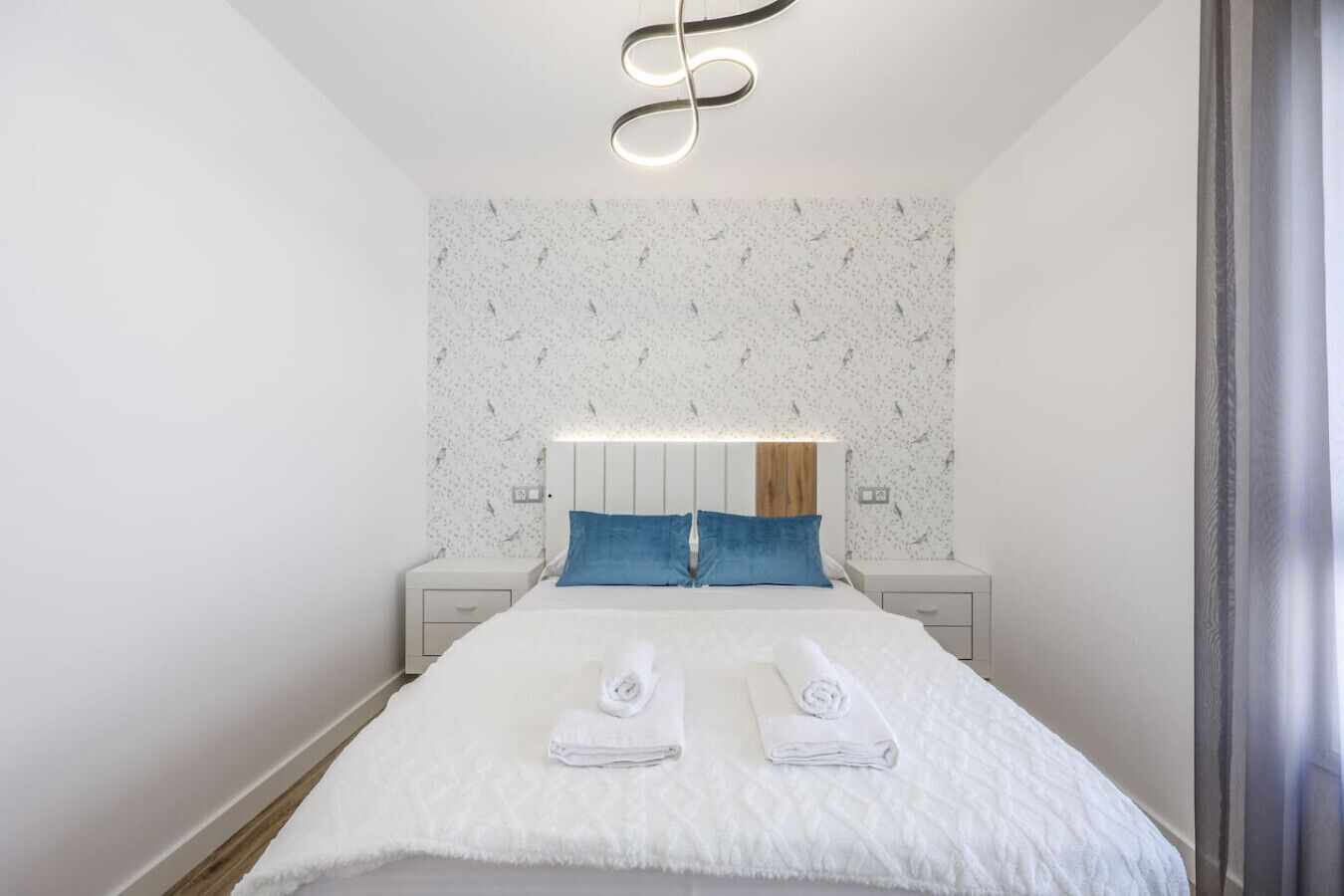 Una habitación de hotel moderna con cama, dos mesitas de noche, cabecero y una lámpara de techo original.