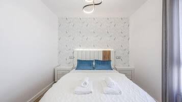 Una habitación de hotel moderna con cama, dos mesitas de noche, cabecero y una lámpara de techo original.