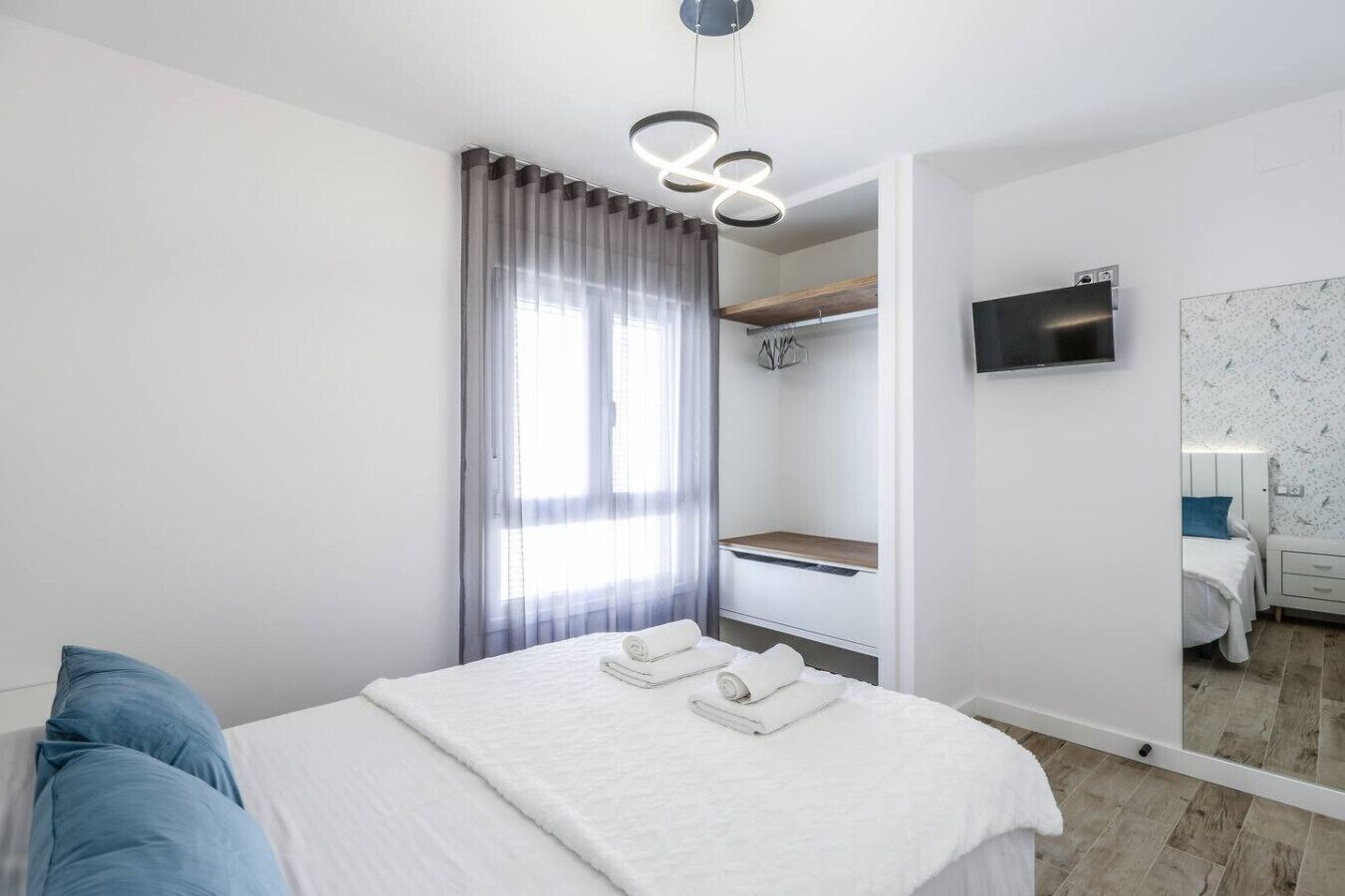Een moderne hotelkamer met een bed, televisie, spiegel en raam met gordijnen.