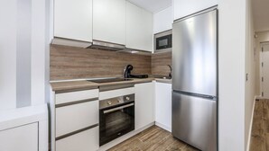 A compact kitchen with white cabinets, a stainless steel refrigerator, a microwave, a stove, and a wooden backsplash.