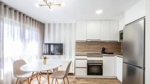 A modern kitchen with white cabinetry, a stainless steel refrigerator, a built-in oven, and a dining area with a round table and chairs.