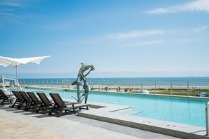 A poolside area with lounge chairs, a dolphin statue, and a view of the ocean. - Blue Horizon | Incredible views | Resort Amenities (Galveston)