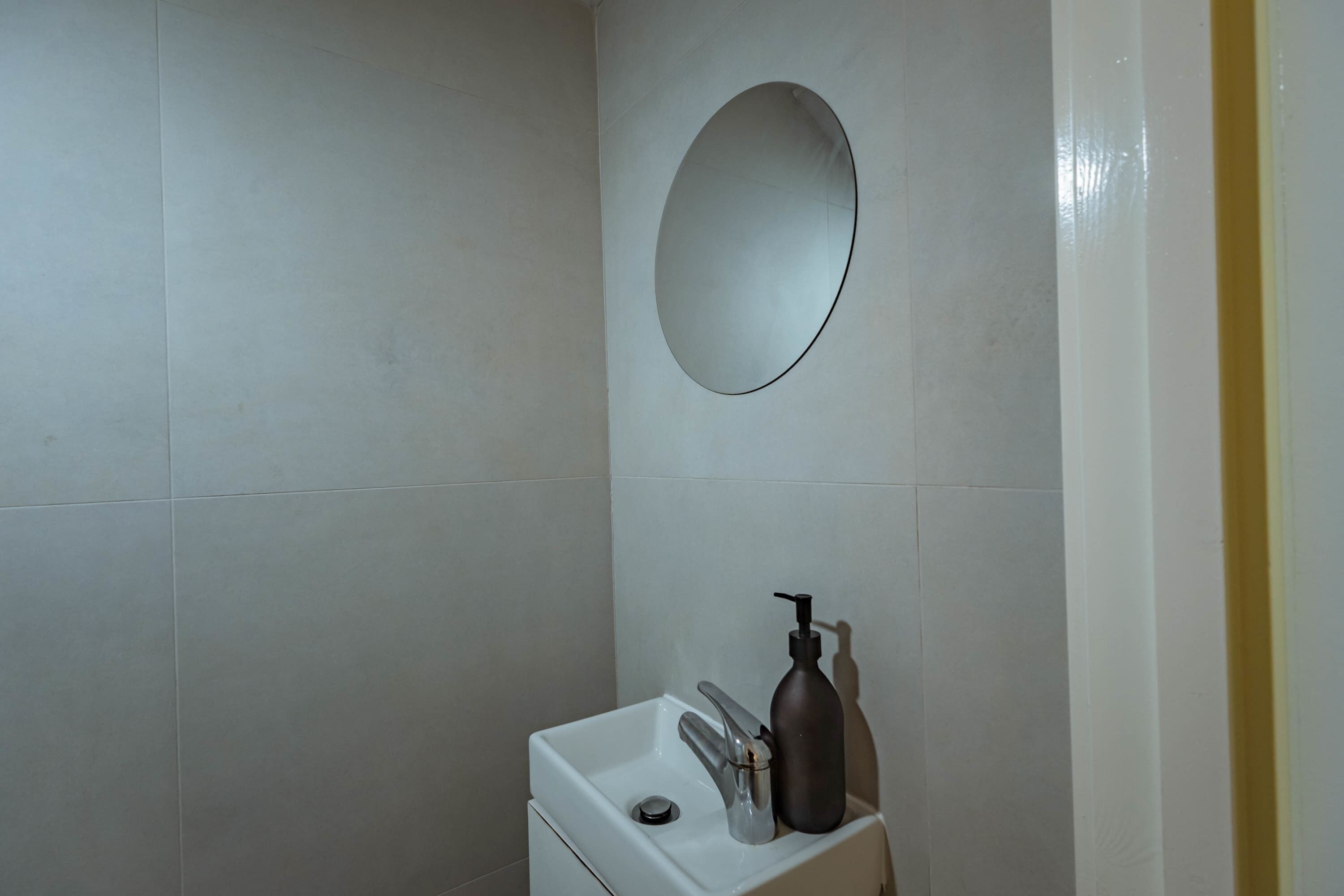 A bathroom with a white sink, a mirror, and a soap dispenser.