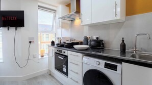 A modern kitchen with white cabinets, a built-in oven, a dishwasher, and a sink. - Bright 3BR Duplex Steps from Shops & Dining (Cardiff)