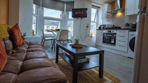 A modern living room with a leather sofa, a coffee table, and a TV mounted on the wall displaying 'NETFLIX'. - Bright 3BR Duplex Steps from Shops & Dining (Cardiff)