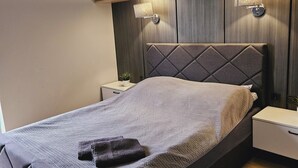 Ein modernes Schlafzimmer mit Bett, Nachttischen, einem Wandregal und einer Wandlampe.