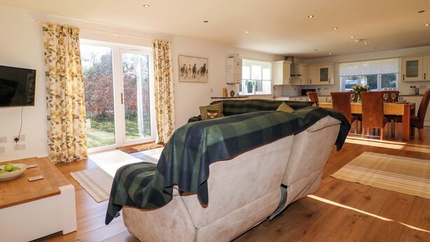 A living room with a sofa, a dining table with chairs, a kitchen area, and a sliding glass door leading to a garden. - Snowdrop Cottage (Maidstone)
