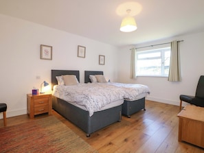 A double bed with a patterned bedspread, a bedside table with a lamp, a chair, and a window with curtains. - Snowdrop Cottage (Maidstone)