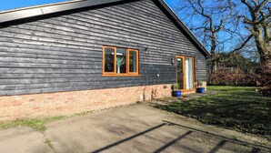 A single-story building with a dark wooden exterior, a brick foundation, and a small front porch with potted plants. - Snowdrop Cottage (Maidstone)
