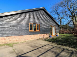 A single-story building with a dark wooden exterior, a brick foundation, and a small front porch with potted plants. - Snowdrop Cottage (Maidstone)