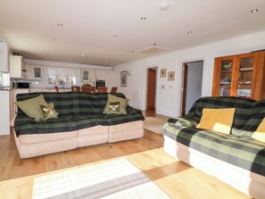 A living room with a sofa set, a kitchen in the background, and a door leading to another room. - Snowdrop Cottage (Maidstone)