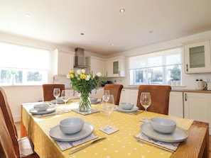 A dining area with a table set for four, white cabinets, and a window with a view. - Snowdrop Cottage (Maidstone)