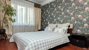 A bedroom with a bed, curtains, a potted plant, and a floral wallpaper.