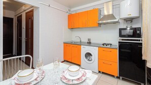 A compact kitchen with orange cabinets, a washing machine, a microwave, and a stove.