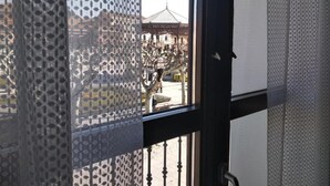 A view through a window with a patterned curtain, a metal gate, and a building with a traditional roof in the background. - Spacious 4-bedroom condo in tranquil Alcalá de Henares -One-Bedroom Apartment (Alcalá de Henares)