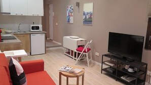 A compact living space with a kitchenette, a television, a red sofa, and a small table. - Spacious 4-bedroom condo in tranquil Alcalá de Henares -One-Bedroom Apartment (Alcalá de Henares)