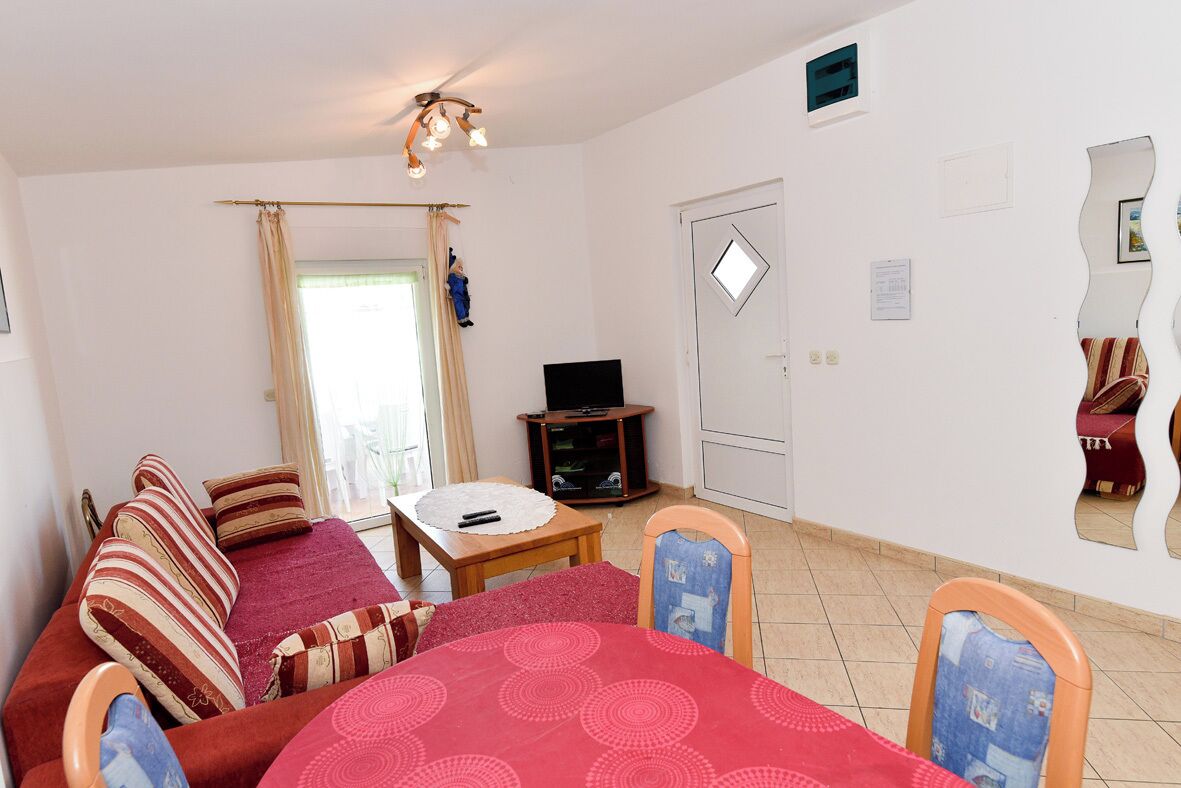 Ein Wohnzimmer mit einer Couch, einem Esstisch, einem Fernseher und einer Tür.