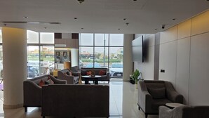 A modern hotel lobby with sofas, a reception desk, a TV, and large windows. - Palette Ninty (Riyadh)