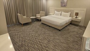 A modern hotel room with a large bed, two armchairs, a small table, and a large window with curtains. - Palette Ninty (Riyadh)