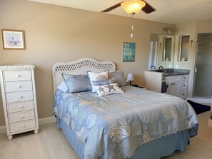A bedroom with a bed, a dresser, a ceiling fan, a bathroom with a shower, and a wall with a framed picture. - Cozy 2-bedroom/2 bath Condo in beautiful Ft Myers Florida. Many amenities! (Fort Myers)