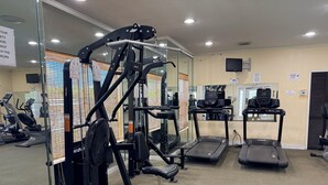 Ein Fitnessstudio mit Trainingsgeräten, Laufbändern und einer Spiegelwand.