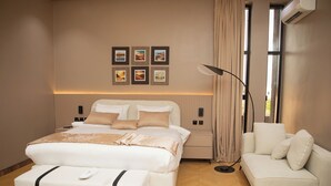 Une chambre moderne avec un grand lit, des tables de chevet, un canapé et un climatiseur fixé au mur.