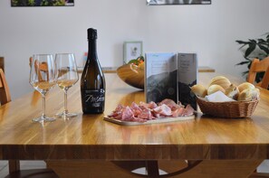 A wooden table with two wine glasses, a bottle of Prosecco, a plate of cured meats, a basket of bread, and a brochure. - Simply Home – Elegant Stay near Treviso & Prosecco Hills (Spresiano)