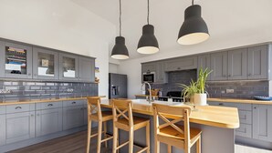 Eine moderne Küche mit grauen Schränken, einer Holztischinsel mit Barhocker und Pendelleuchten.