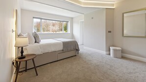 Quarto com cama, janela, luminária e um banquinho.