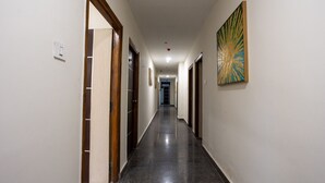 A long, narrow hallway with doors on both sides, a light switch on the left, and a painting on the right wall. - Hotel V Grand (Hyderabad)