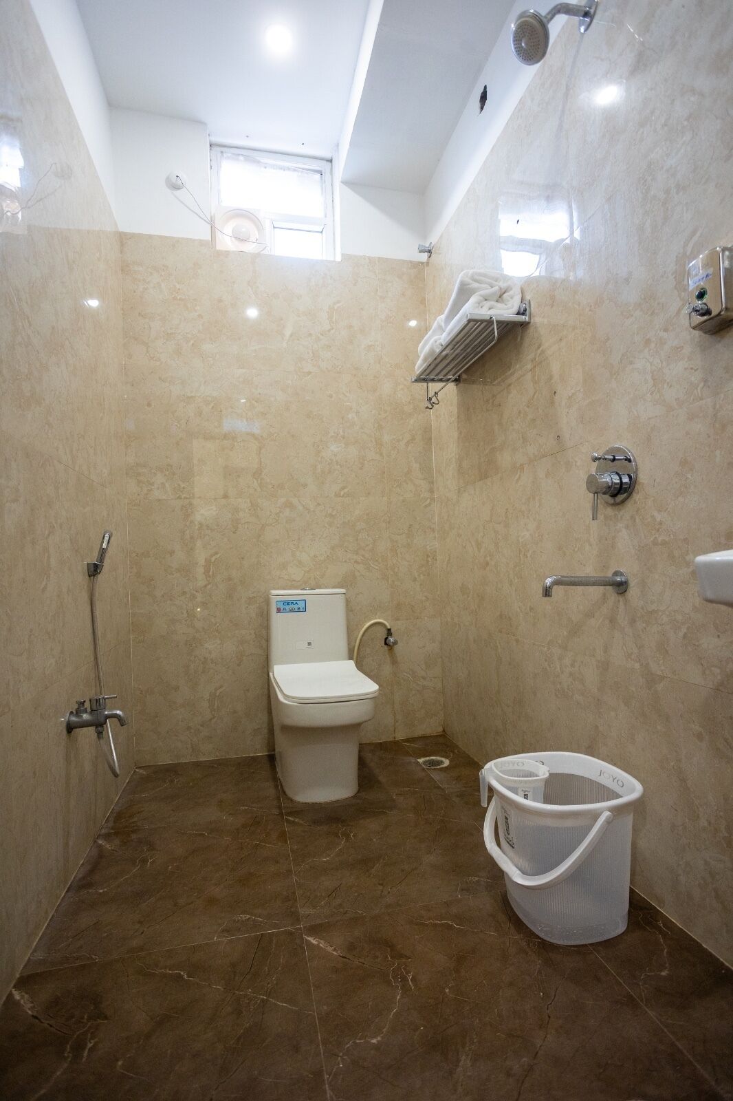 Een badkamer met toilet, douche en een witte emmer.