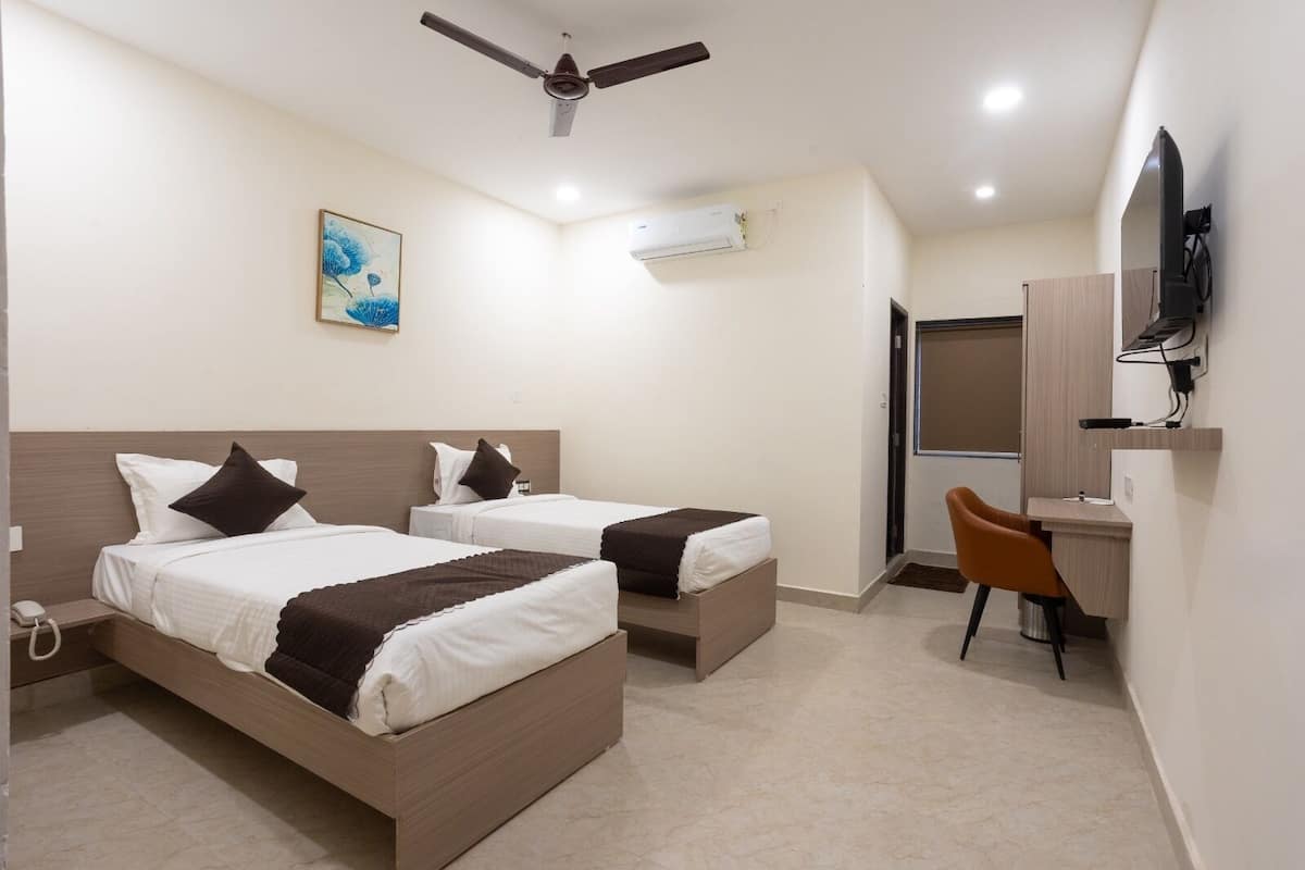 Habitación de hotel con dos camas, un escritorio, una silla, ventilador de techo, unidad de aire acondicionado y un cuadro en la pared.