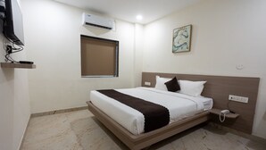 A hotel room with a bed, a bedside table, an air conditioning unit, a power outlet, and a painting on the wall. - Hotel V Grand (Hyderabad)