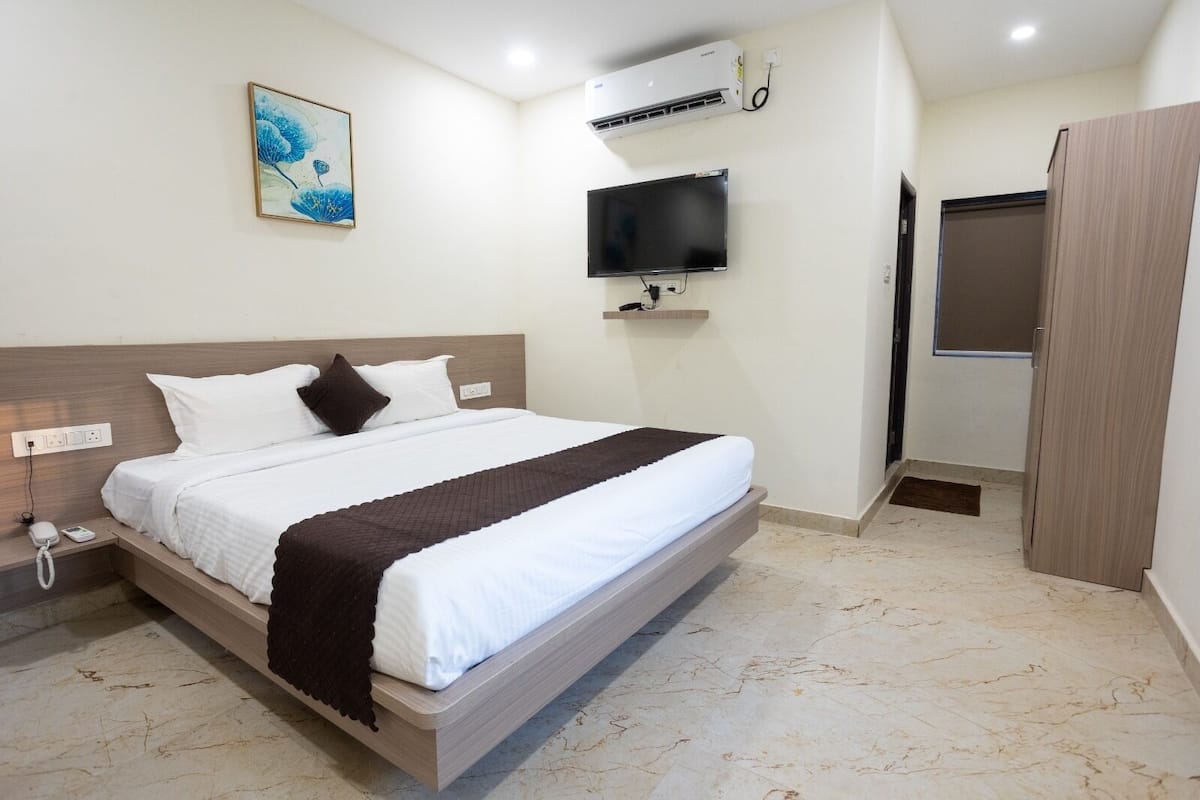 Habitación de hotel con cama, televisión montada, aire acondicionado y un cuadro en la pared.