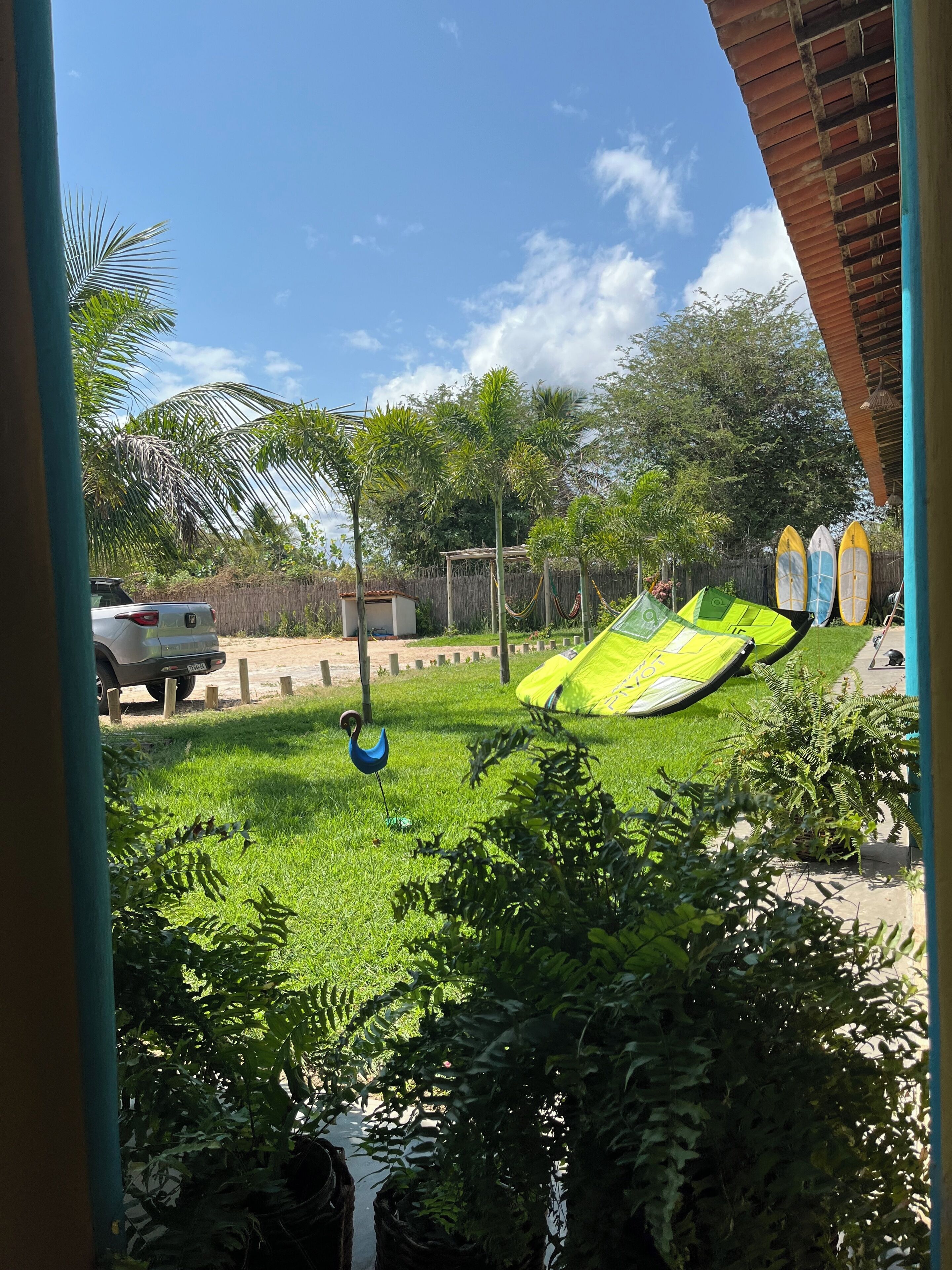Un espacio al aire libre con césped, una hamaca, un coche aparcado y tablas de surf.